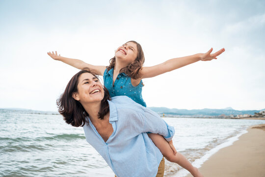 Cheerful woman giving piggyback ride to daughter at beach