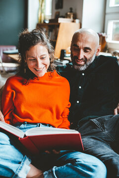 Happy woman sharing book with man sitting at home