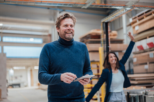 Happy businessman with tablet PC by colleague in workshop