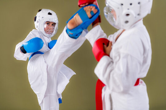 Karate practitioner launches a powerful side kick toward a standing opponent who holds a defensive guard position, capturing full leg extension and body rotation during an active sparring session.