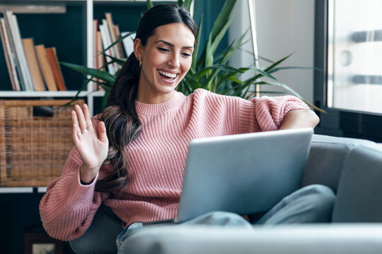 Freelancer waving during a laptop videocall on a cozy sofa