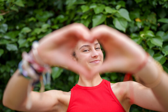 Smiling girl framing face with heart hand gesture in garden