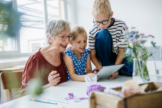 Smiling grandmother playing on tablet with grandchildren at home