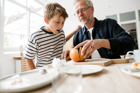 Father opening a grapefruit for his son at home in the morning
