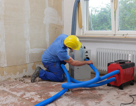 Worker fixing hose of dehumidifier in an apartment which is damaged by flooding