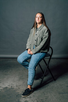 Woman sitting on chair in front of gray backdrop