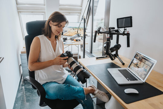 Smiling photographer checking camera sitting on chair in studio