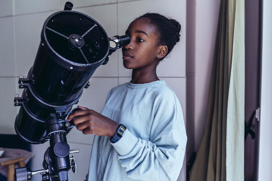 Pre-adolescent girl looking through telescope at home