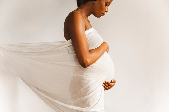 Young pregnant woman covered in white sheet in front of wall