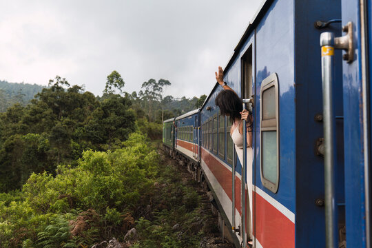Woman leaning out of a moving train in lush Sri Lanka