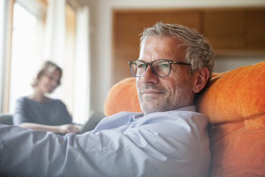 Man relaxing in armchair with wife in background