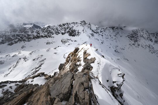 Mountaineer descending the narrow ridge of Piz Laviner, view of mountain panorama in wintry mountain landscape with dramatic clouds, Grisons Haute Route, Albula Alps, Rhaetian Alps, Grisons, Eastern Switzerland, Switzerland