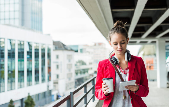 Young woman with coffee to go, headphones and phablet in parking garage