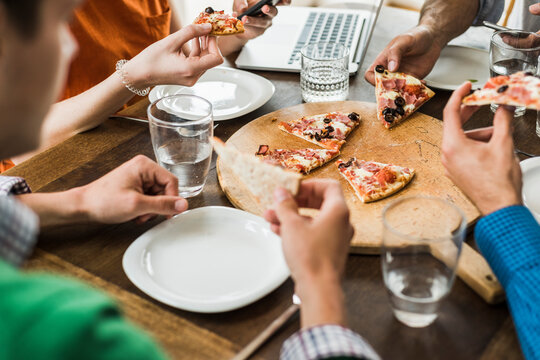 Colleagues at table with cell phone and laptop having a pizza
