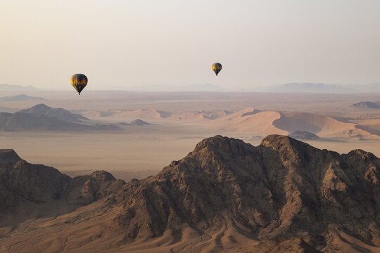 Two hot-air balloons above an arid plain and isolated mountain ridges at the edge of the Namib Desert. Aerial view from another balloon. Namibia