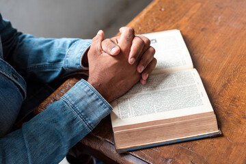 Naklejka premium Person in denim jacket with hands clasped over an open book on a table.
