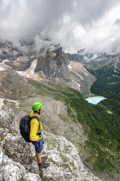 Young man, mountaineer on a fixed rope route, Via Ferrata Vandelli, view of Lago di Sorapis, Sorapiss circuit, mountains with low clouds, Dolomites, Belluno, Italy