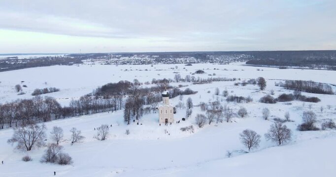 Cinematic aerial pull-back shot revealing the historic Church of the Intercession on the Nerl in a snowy winter landscape near Bogolyubovo, Russia