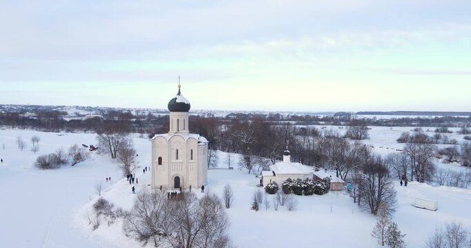 Cinematic aerial shot pushing forward towards the solitary Church of the Intercession on the Nerl in a snowy winter landscape near Bogolyubovo, Russia