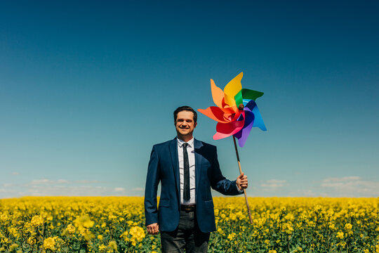 Smiling businessman holding colorful pinwheel in rapeseed field