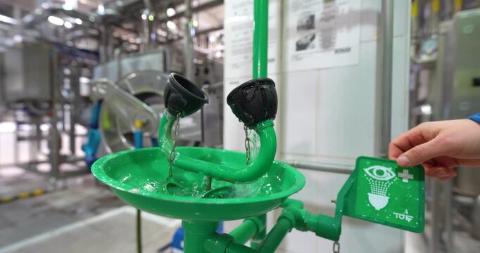 Steady close-up shot of a factory worker's hand activating a green emergency eyewash station in an industrial manufacturing plant