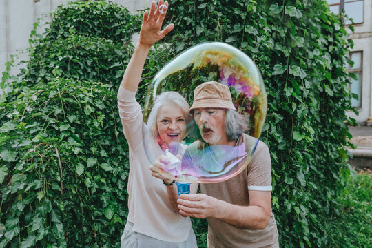 Happy mature woman enjoying by senior man making bubbles in park