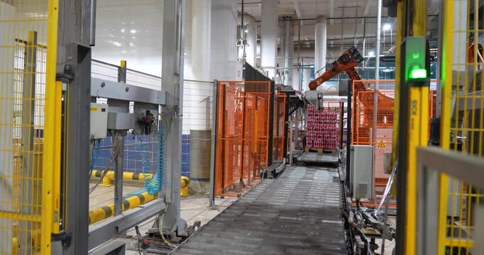 Steady shot of an automated orange industrial robotic arm palletizing packaged beverages behind a safety fence in a modern manufacturing plant