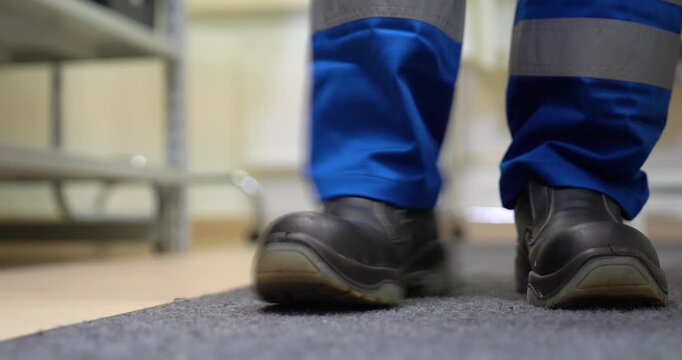 Steady close-up shot of a factory worker changing into black protective safety shoes on a mat before starting a shift