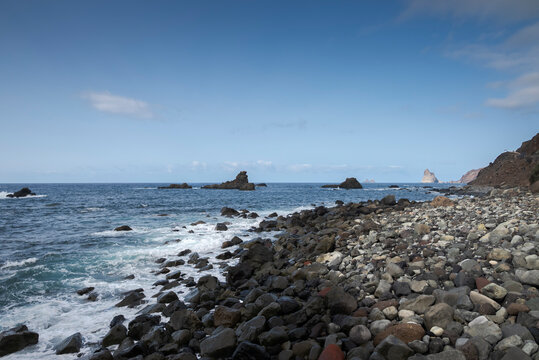 Rocky beach on the north coast of Tenerife, Canary Islands, Spain, at Almaciga beach, with dark volcanic stones, blue ocean waves, and a clear sky.