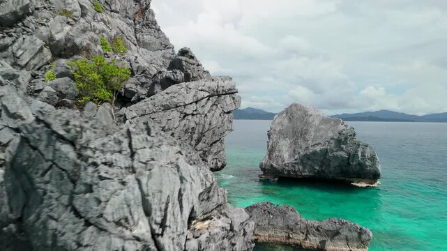 Close aerial flyover past Twin Rocks El Nido revealing dramatic rugged limestone cliffs rising from vivid turquoise sea with distant islands on horizon