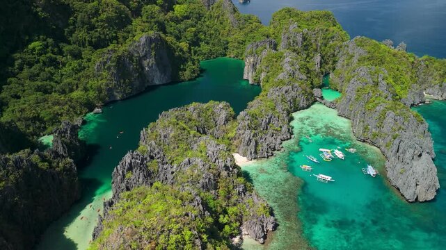 Aerial parallax above Big Lagoon and Small Lagoon revealing jagged limestone karst islands turquoise reef and moored tour boats at Miniloc Island of El Nido Palawan Philippines