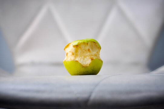 Close up shot of an abandoned bitten green apple starting to brown and oxidize on a modern white quilted leather chair