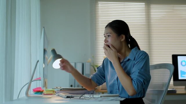 Young Asian woman receiving good news on her computer. She feels excited, celebrates victory, and expresses gratitude while working overtime