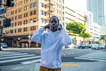 Person in a white hoodie stands at a city intersection, adjusting hood. © Rawpixel.com