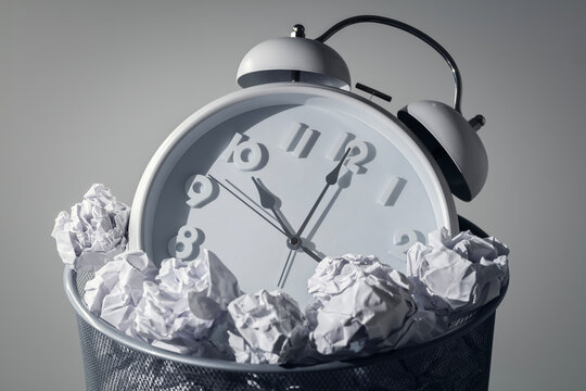 Wasting time, procrastination, delay or being unproductive, alarm clock in a wastepaper bin