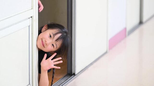 教室のドアから顔を出して笑顔で手を振る女子小学生たち