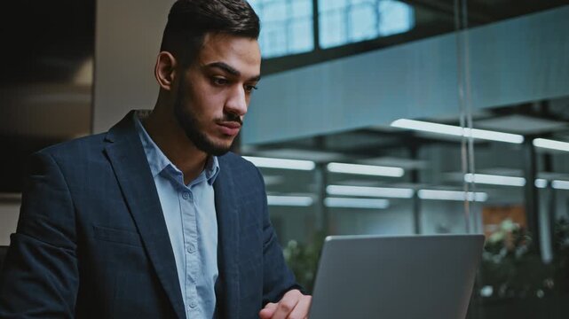 Focused Young Asian Man Engaged With Laptop In Modern Office Environment, Concentrating On Work. Professional Setting Reflecting A Business Concept With Clear Goal Orientation.