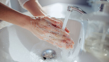 Fototapeta premium A closeup of hands washing with rich soap bubbles under a running faucet in a clean bathroom sink. Perfect for campaigns on personal hygiene, wellness, and health protection.