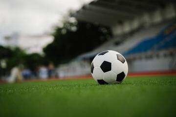Fototapeta premium A soccer ball rests on a green field with a blurred stadium background, representing football competition, teamwork, athletic performance, and the spirit of the game.