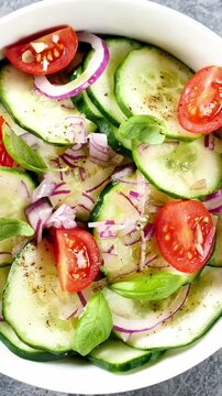 macro shot of a fresh cucumber salad with cherry tomatoes red onion and basil leaves in a white bowl