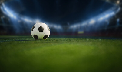 A soccer ball rests on a green field with a blurred stadium background, representing football competition, teamwork, athletic performance, and the spirit of the game. © Witoon