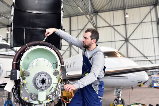 Aircraft mechanic repairs an aircraft engine in an airport hangar