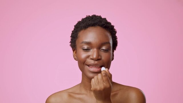 Smiling Young Black Woman Applying Lip Balm To Lips, Showing Happy Emotion, At Home Setting, Indoor. Skincare Concept Focused On Lip Care And Beauty Routine