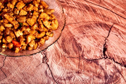 Sweet and savory tempe orek indonesian dish on transparent plate isolated on horizontal wooden brown background with copy space.