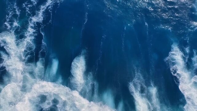 Ocean waves and aerial top down view of deep blue water. White foam patterns on surface. Static camera shot of crashing sea. Ideal for backgrounds.