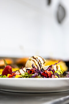 Fruit salad dessert with ice cream scoop, raspberry, and chocolate drizzle on plate
