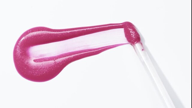 Close up of wand swipe pink shimmering lip gloss texture, satisfying make up lipgloss brush stroke. Cosmetic product swatch background