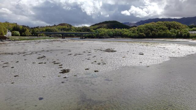 Drone orbit clip showcasing the Morar Bridge spanning the wide tidal river and beach flats, backdropped by rolling hills in the Scottish Highlands.