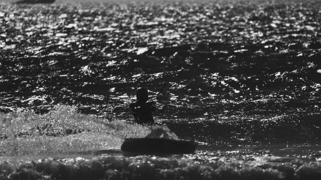 Kite surfer rides waves at the beach during sunset in black and white