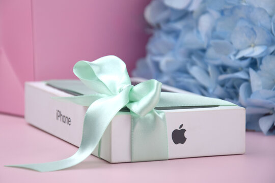 The box with an iPhone 15 Pro Max phone with a bow as a gift on a pink background.